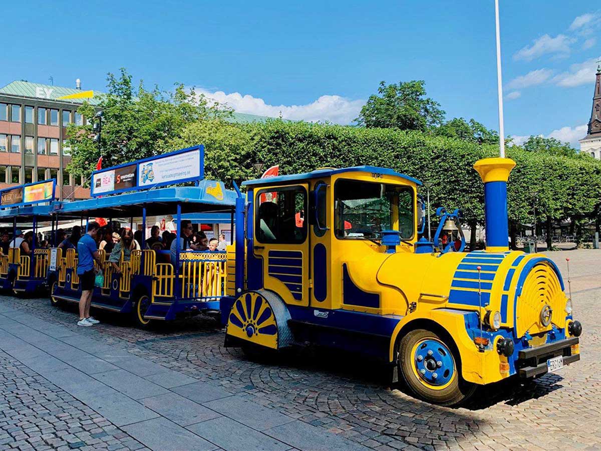 Yellow and blue Gopo tourist train with passengers in a town square